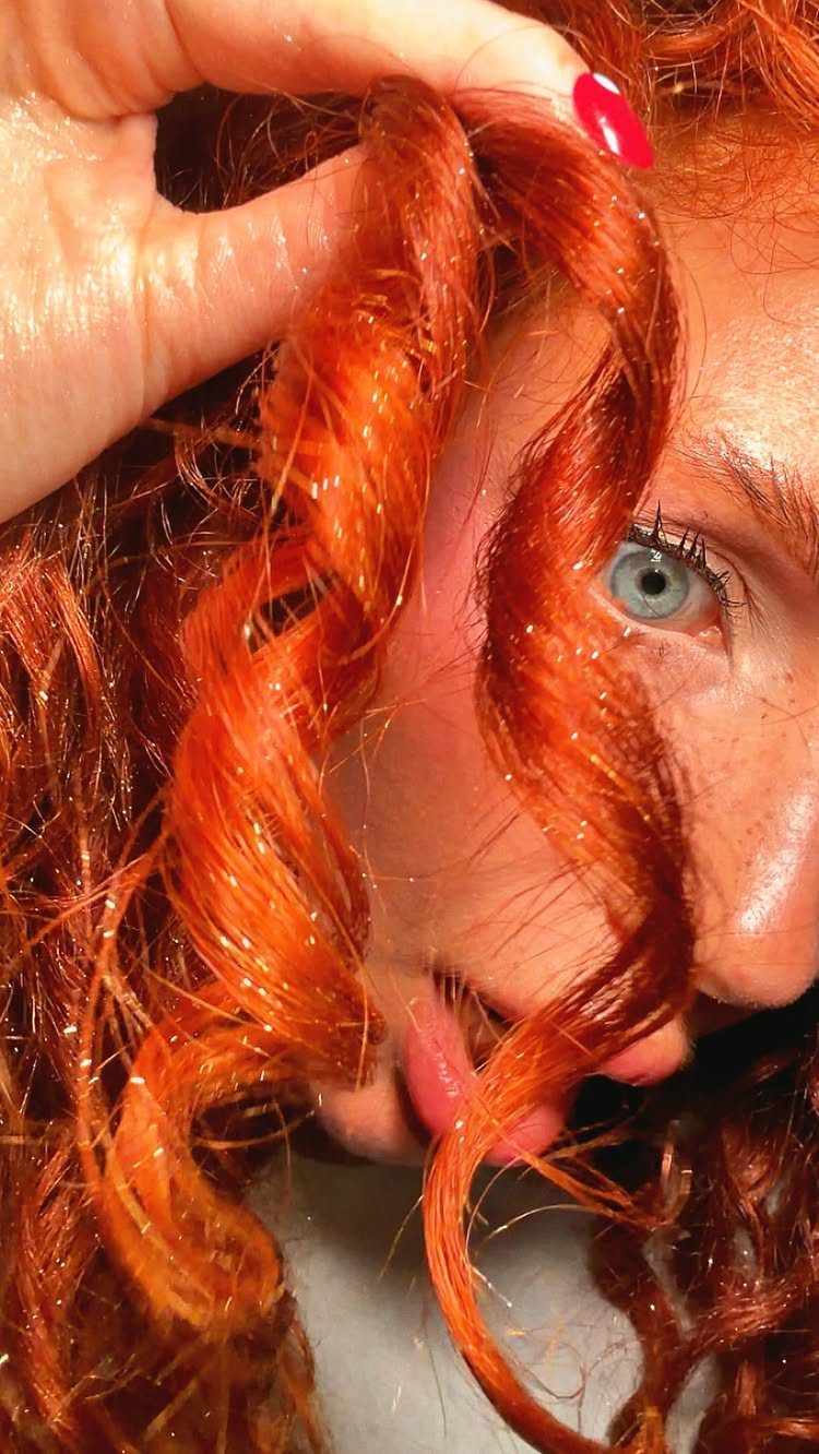 Long 3c Curly Hair Looks, Color and Updos: 15 Picks 1 Vibrant red curly hair with a single spiral curl held by a hand.