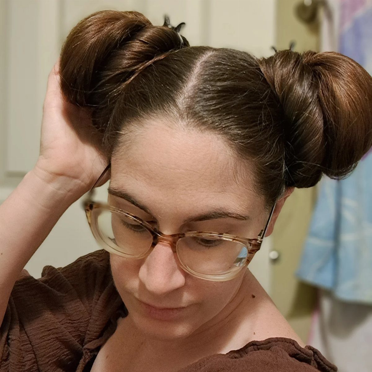 16 Long Hair Hairstyles for Party Looks You Can Copy 13 Woman with brown hair styled in two high space buns wearing glasses.