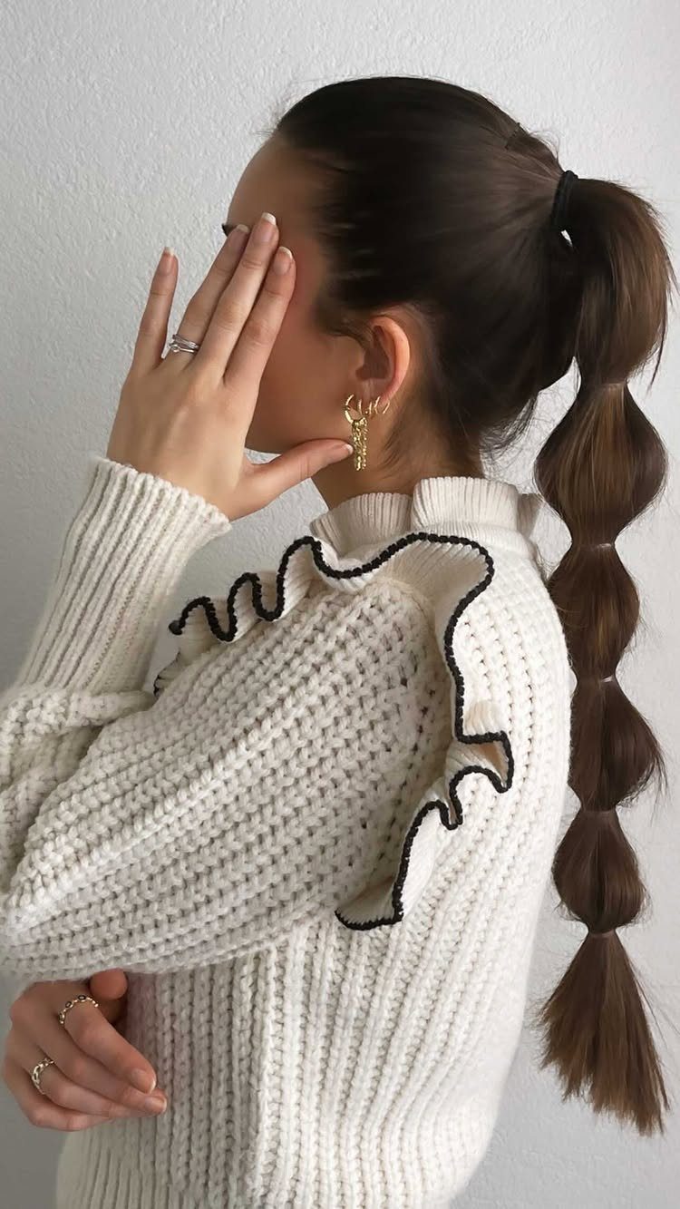20 Long Hair Hairstyles for Work, From Buns to Braids 7 Woman with brown hair in a bubble ponytail wearing a white ruffled sweater.