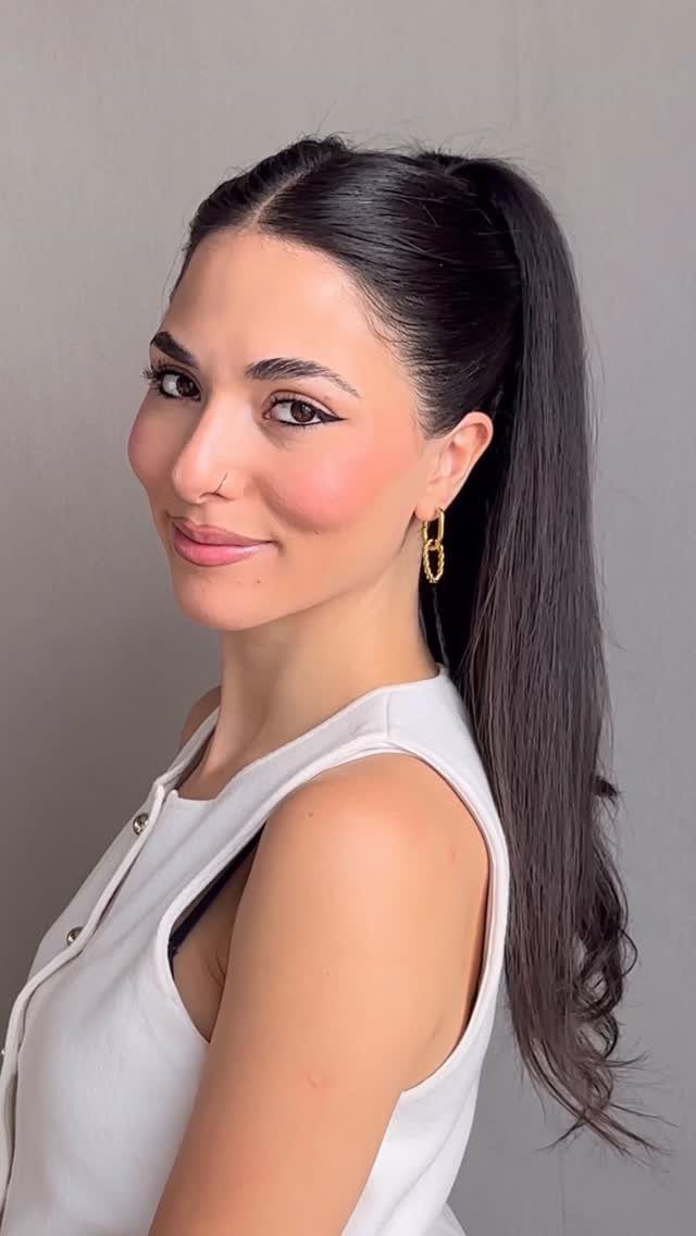 20 Long Hair Hairstyles for Work, From Buns to Braids 3 Woman with long dark hair styled in a high ponytail wearing white top.
