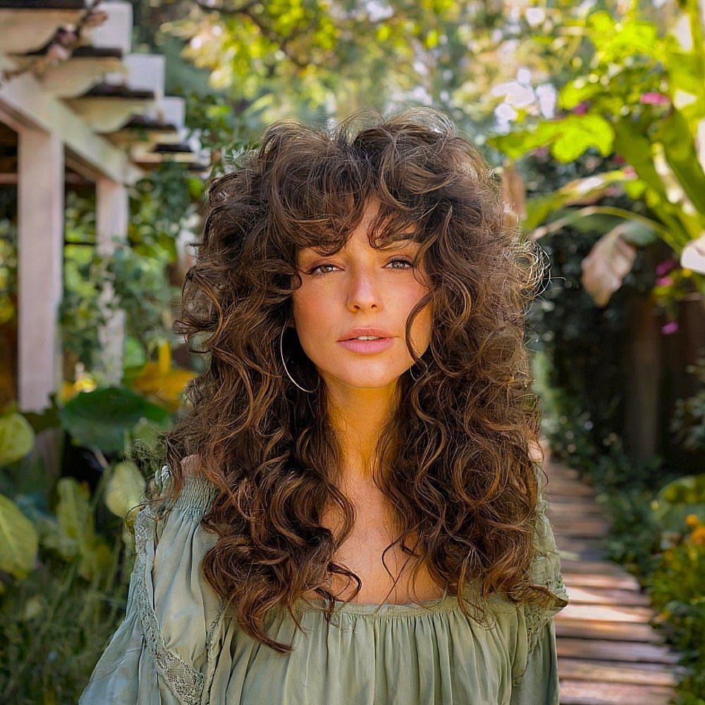 11 Long Loose Hair Ideas for Every Style and Texture 2 Woman with long brown curly hair and curly bangs in a lush garden