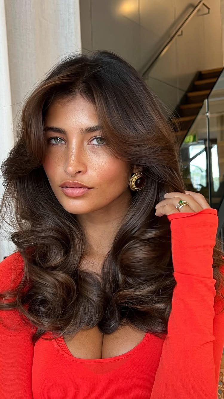 11 Medium Length Curly Hair Hairstyles for Every Look 3 Woman with voluminous brown bouncy blowout waves and a red ribbed top.