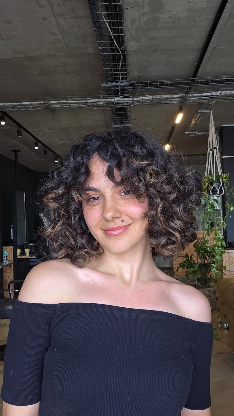 11 Medium Length Curly Hair Hairstyles for Every Look 2 Woman with a defined mid-length curly bob and dark hair wearing black top.