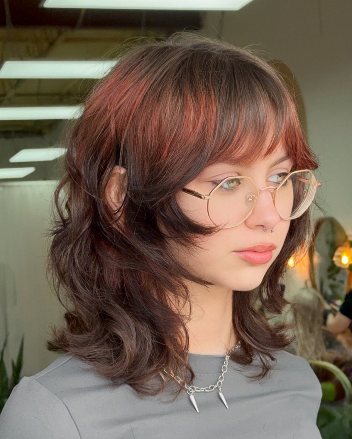 11 Medium Length Curly Hair Hairstyles for Every Look 1 Woman with layered shoulder-length shag curly hair and bangs wearing gold glasses.