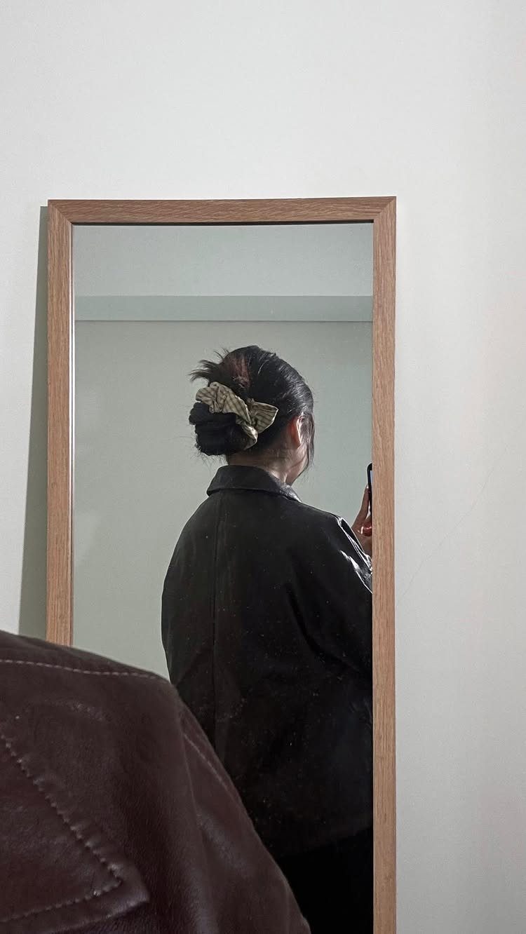 Messy Bun Outfit: 7 Ideas from Jeans to Animal Print 4 Person with a messy bun and leather jacket posing in a mirror