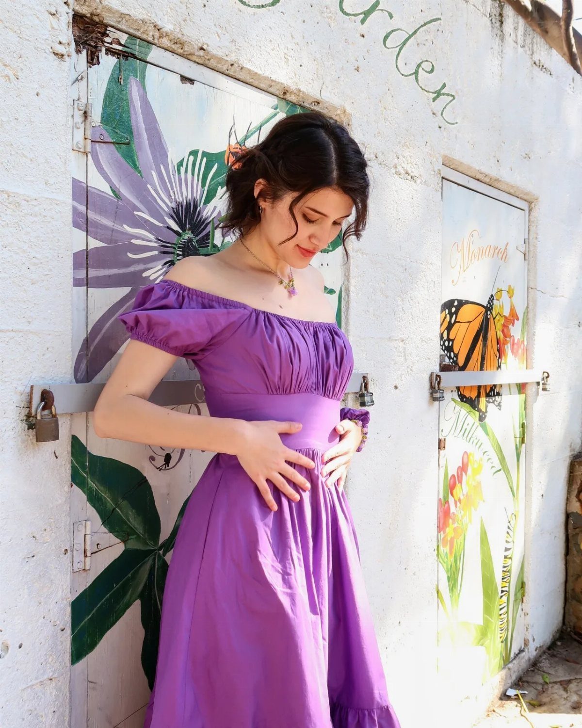 Messy Bun Outfit: 7 Ideas from Jeans to Animal Print 3 Woman with a messy bun wearing a purple off-the-shoulder dress by a mural.
