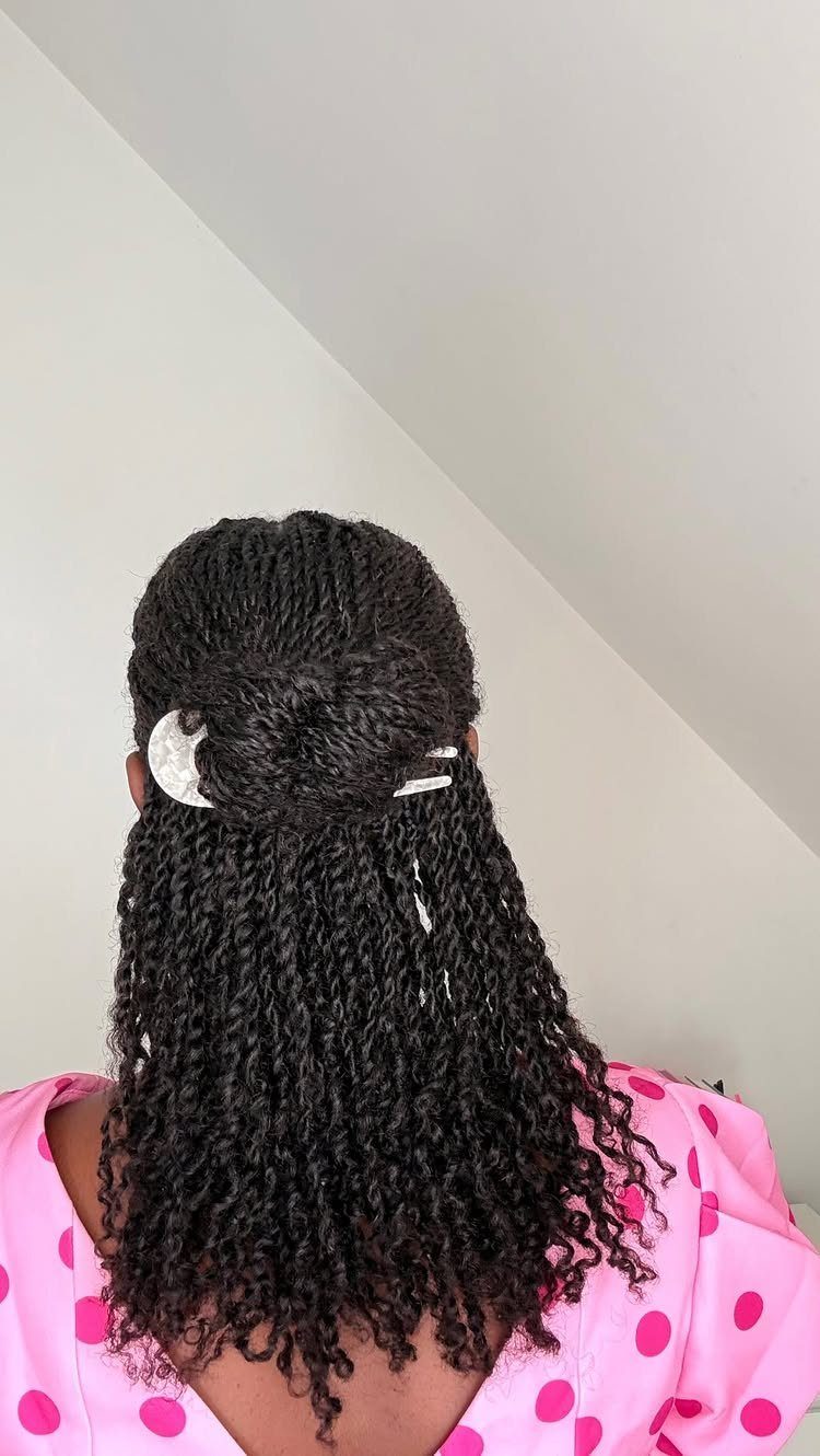 Long black mini twists partially tied in a bun with a white clip.