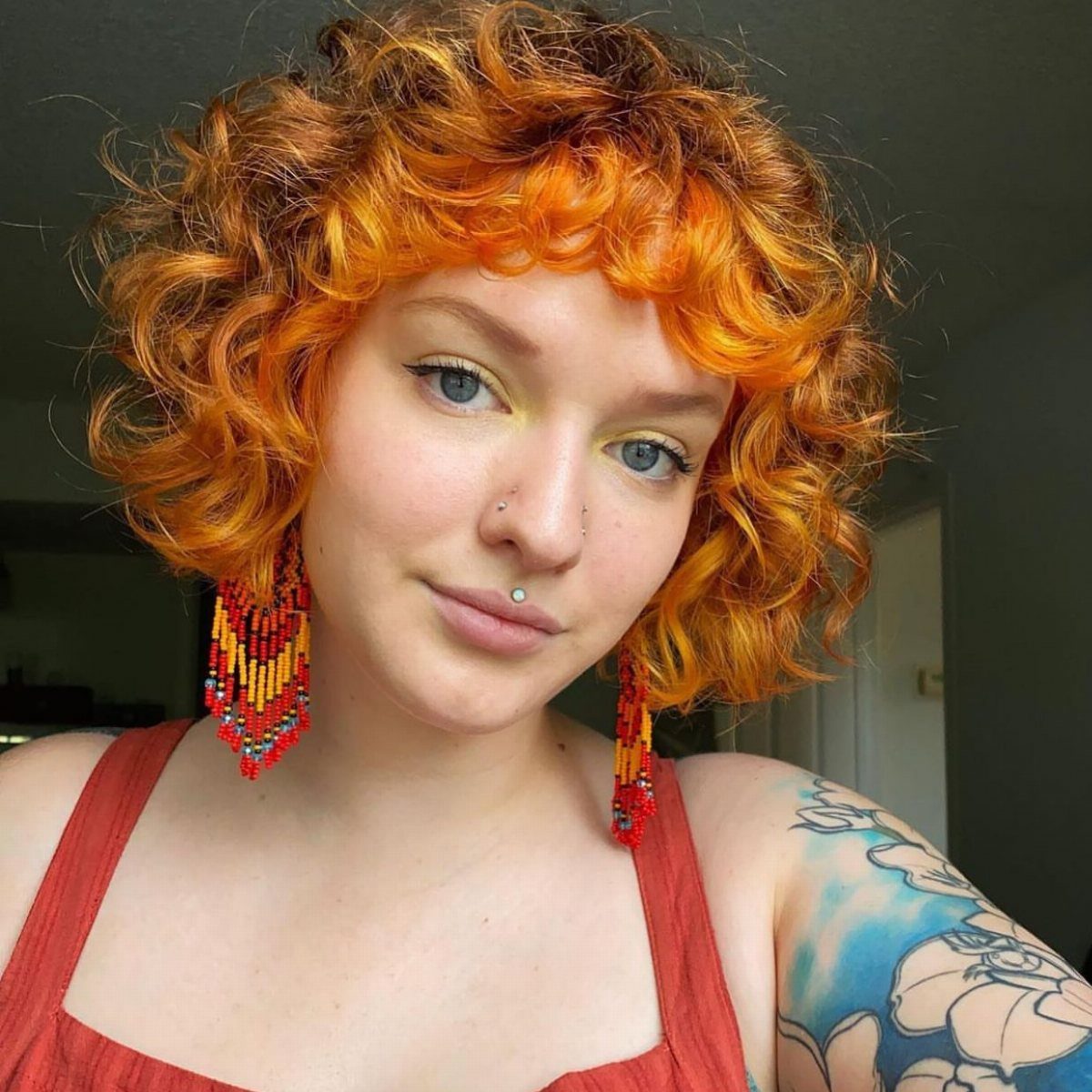17 Natural Curly Hairstyles for Short Hair You Can Wear 13 Person with bright orange curly bob hair and curly bangs wearing red earrings