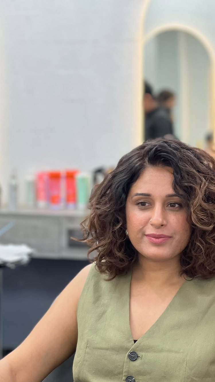17 Natural Curly Hairstyles for Short Hair You Can Wear 9 Woman with a shoulder-length curly bob hairstyle wearing a green sleeveless top.