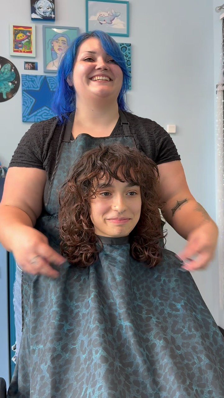 17 Natural Curly Hairstyles for Short Hair You Can Wear 3 Woman with a brown curly shag haircut and bangs posing with her stylist.