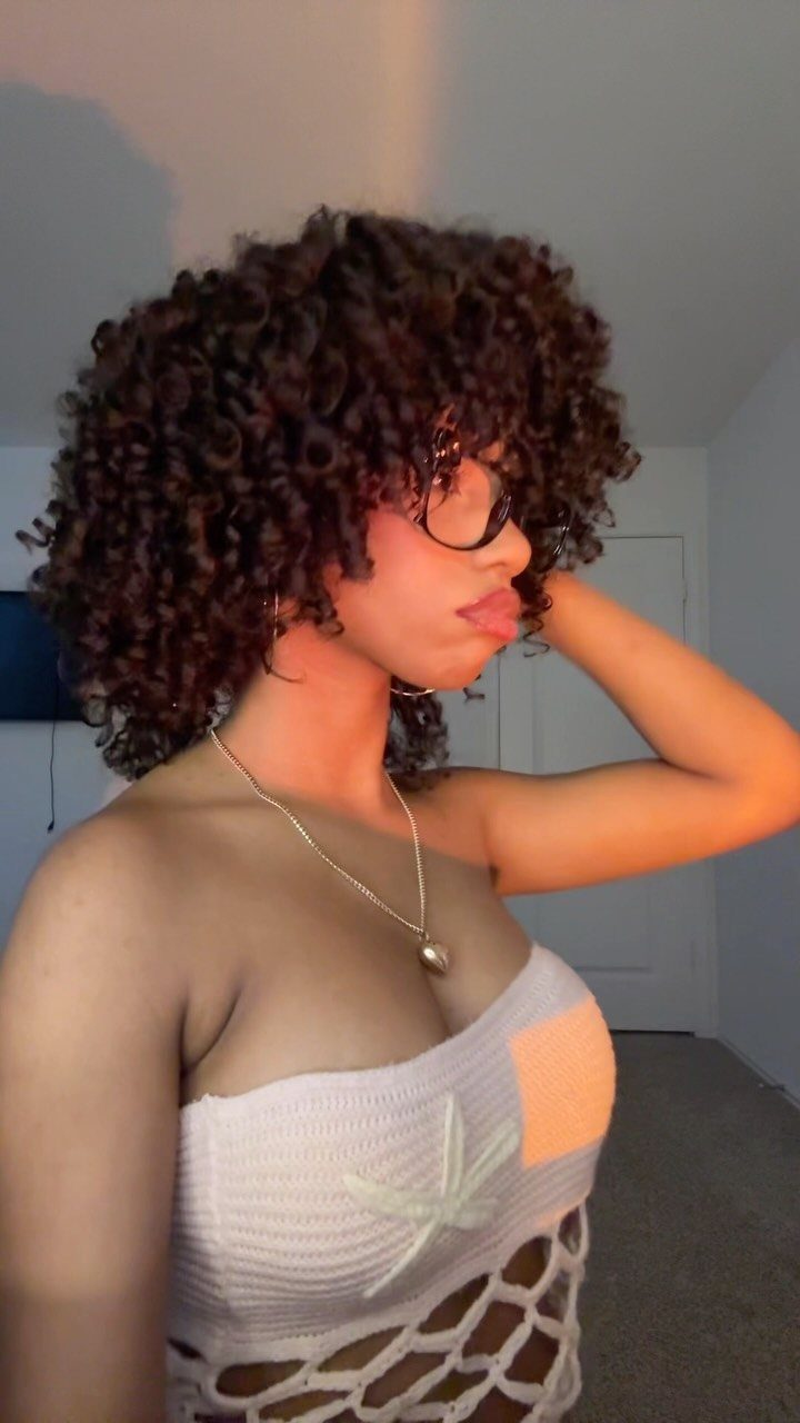 17 Natural Curly Hairstyles for Short Hair You Can Wear 4 Woman with short, voluminous dark brown curly hair wearing glasses and white crochet top.