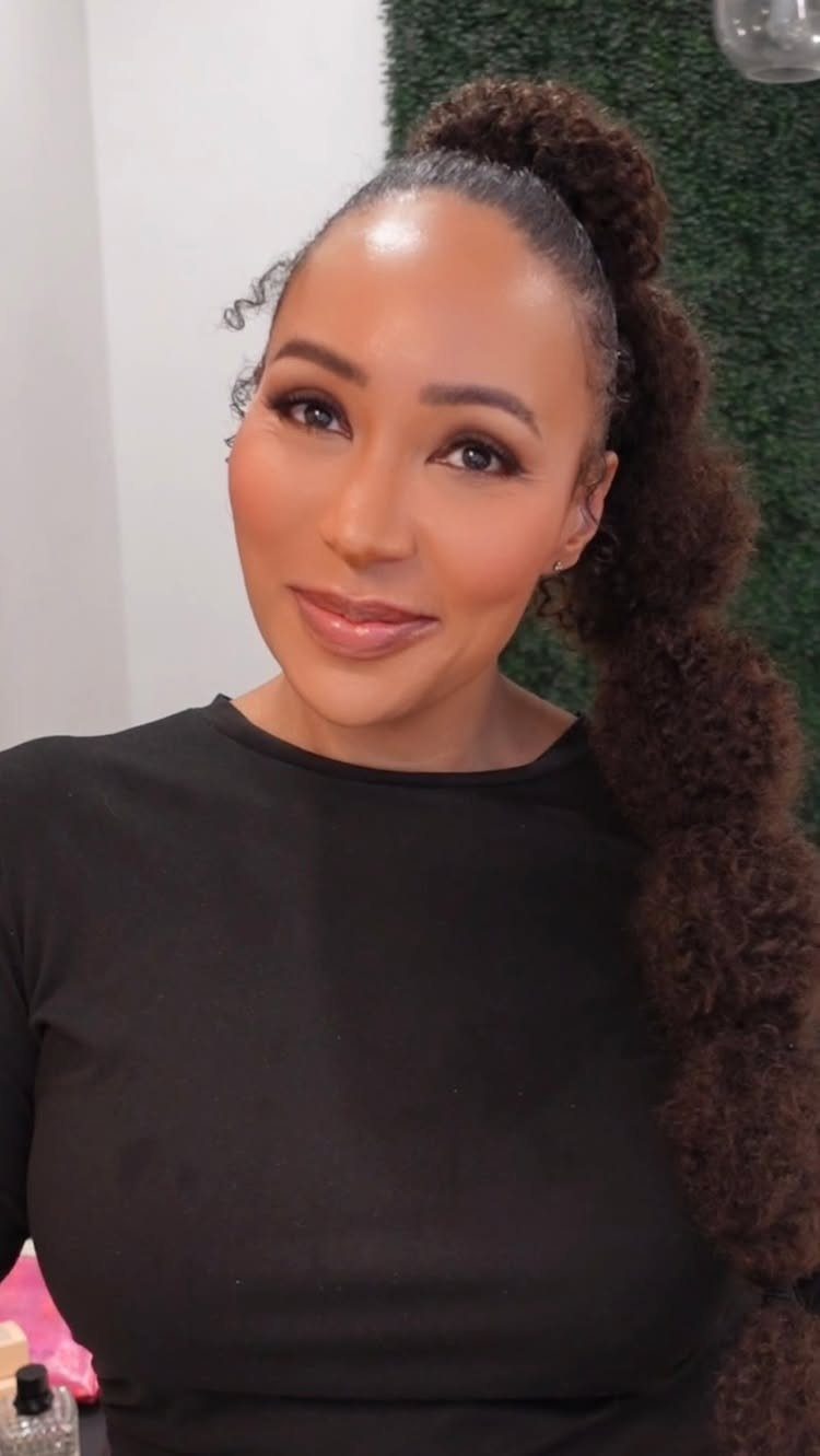 Woman with a high bubble ponytail hairstyle and natural curly brown hair.
