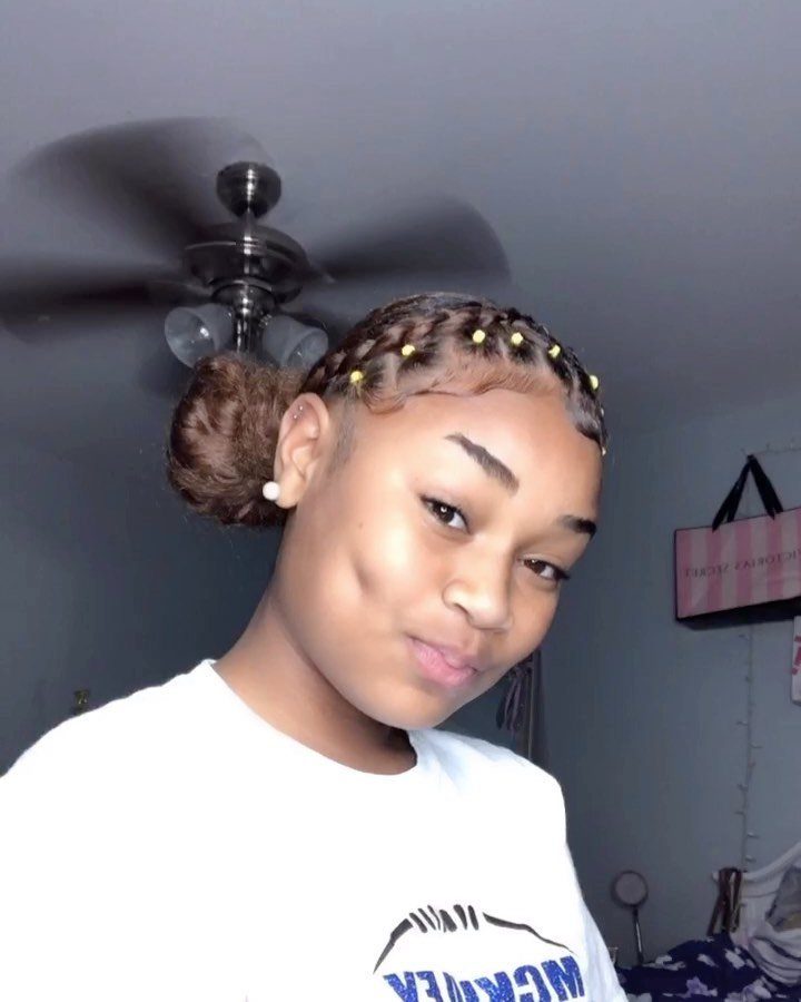 Young woman with cornrow braids and a high curly puff hairstyle with gold beads.