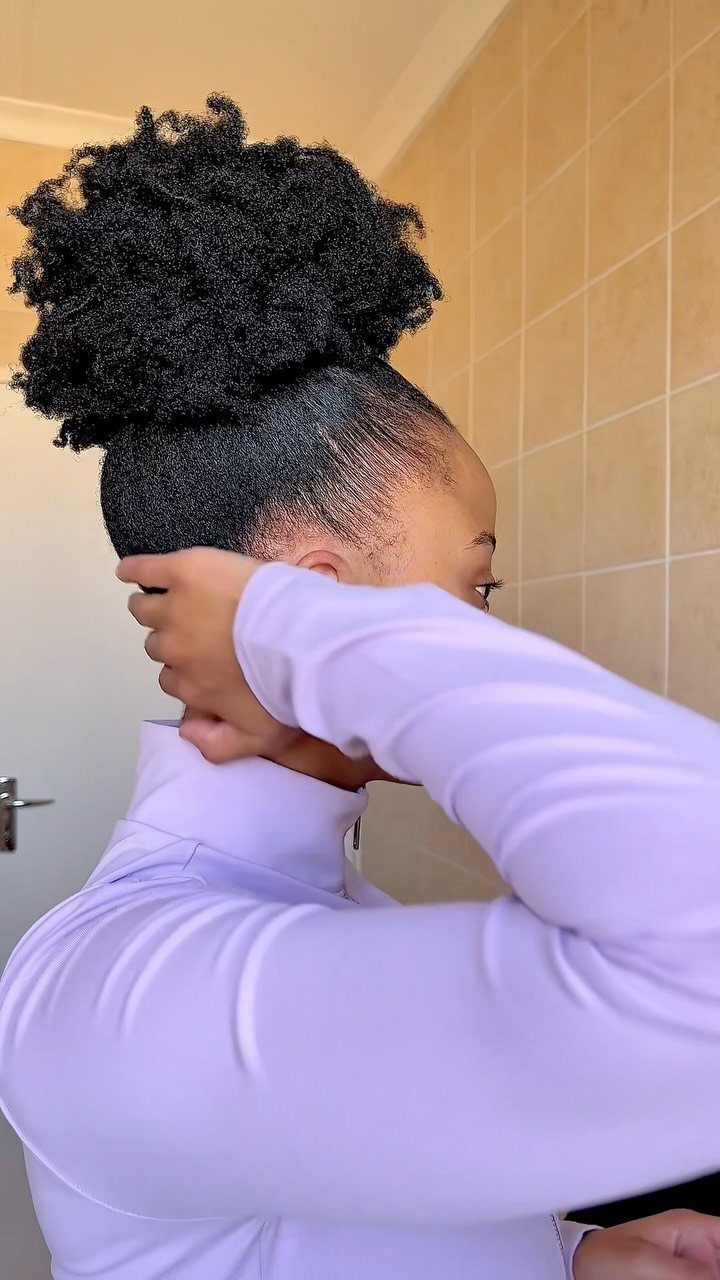 Person with natural hair styled in a high voluminous puff wearing purple shirt