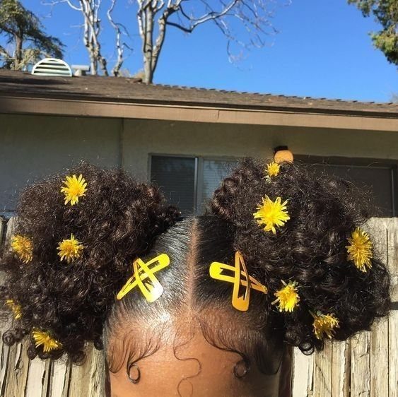 Two high curly hair puffs decorated with yellow flowers and yellow hair clips.