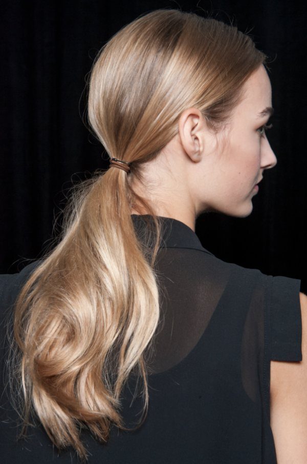 Blonde woman with a low ponytail secured by a brown hair tie.