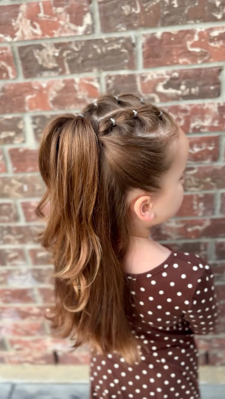 11 Picture Day Hair Ideas for Kids, from Braids to Bows 6 Young girl with a braided high ponytail standing against a red brick wall