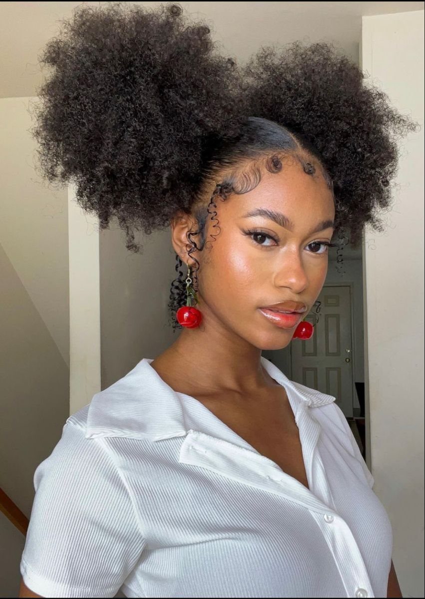 Puff Ball Hairstyle Ideas: 5 Styles With Afro Puffs and Bows 1 Woman with two high afro puffs, wearing a white shirt and cherry earrings.