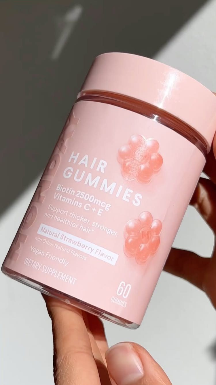 3 Ideas for Quick Hair Growth: Massage, Supplements, Care 2 Pink bottle of hair gummies held by a hand against a bright background.