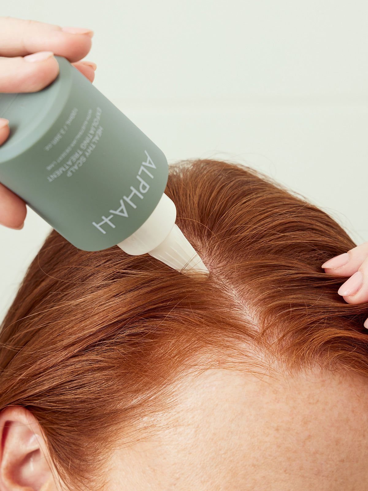 Scalp Care for Dandruff: 3 Ideas to Try at Home 3 Person applying a scalp treatment from a grey bottle to red hair.