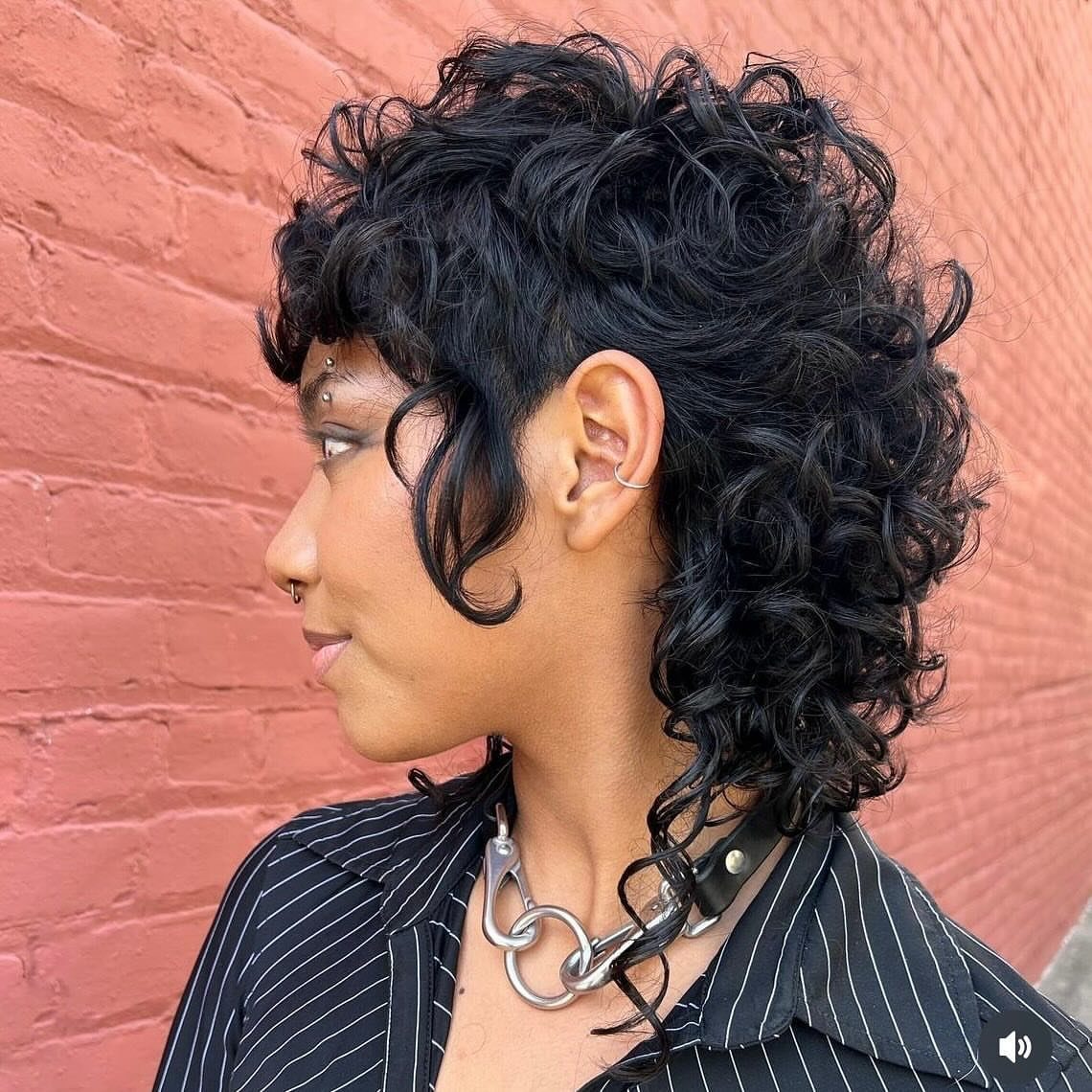 21 Short Curly Hair Styling Ideas for Every Texture 4 Person with a curly mullet hairstyle posing against a red brick wall.