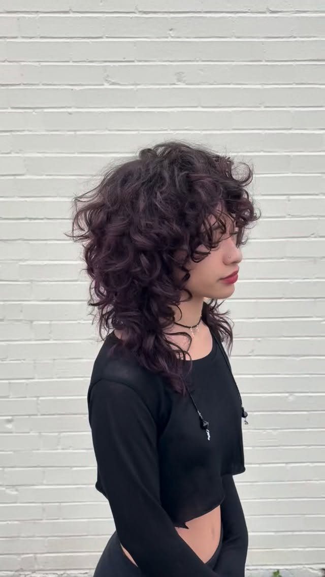 21 Short Curly Hair Styling Ideas for Every Texture 3 Person with a layered curly shag haircut and bangs against a white wall