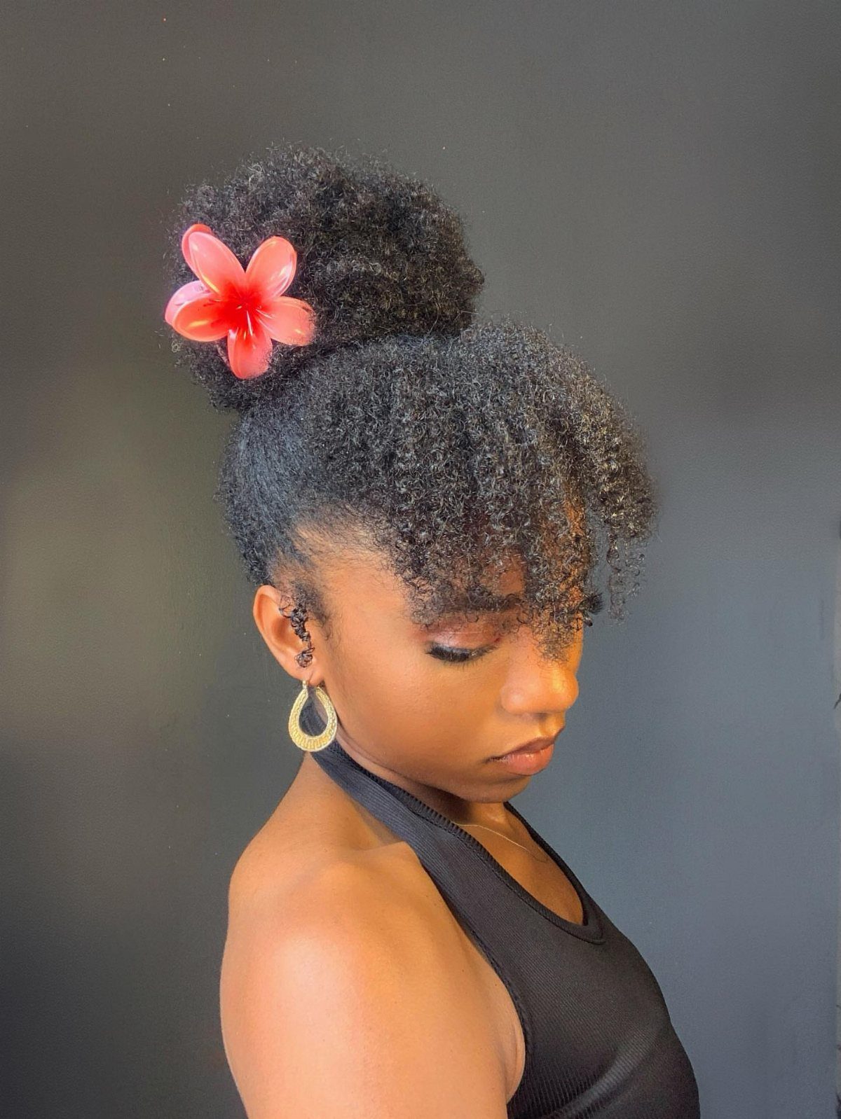21 Short Curly Hair Styling Ideas for Every Texture 19 Woman with short curly black hair in a bun with a red flower.
