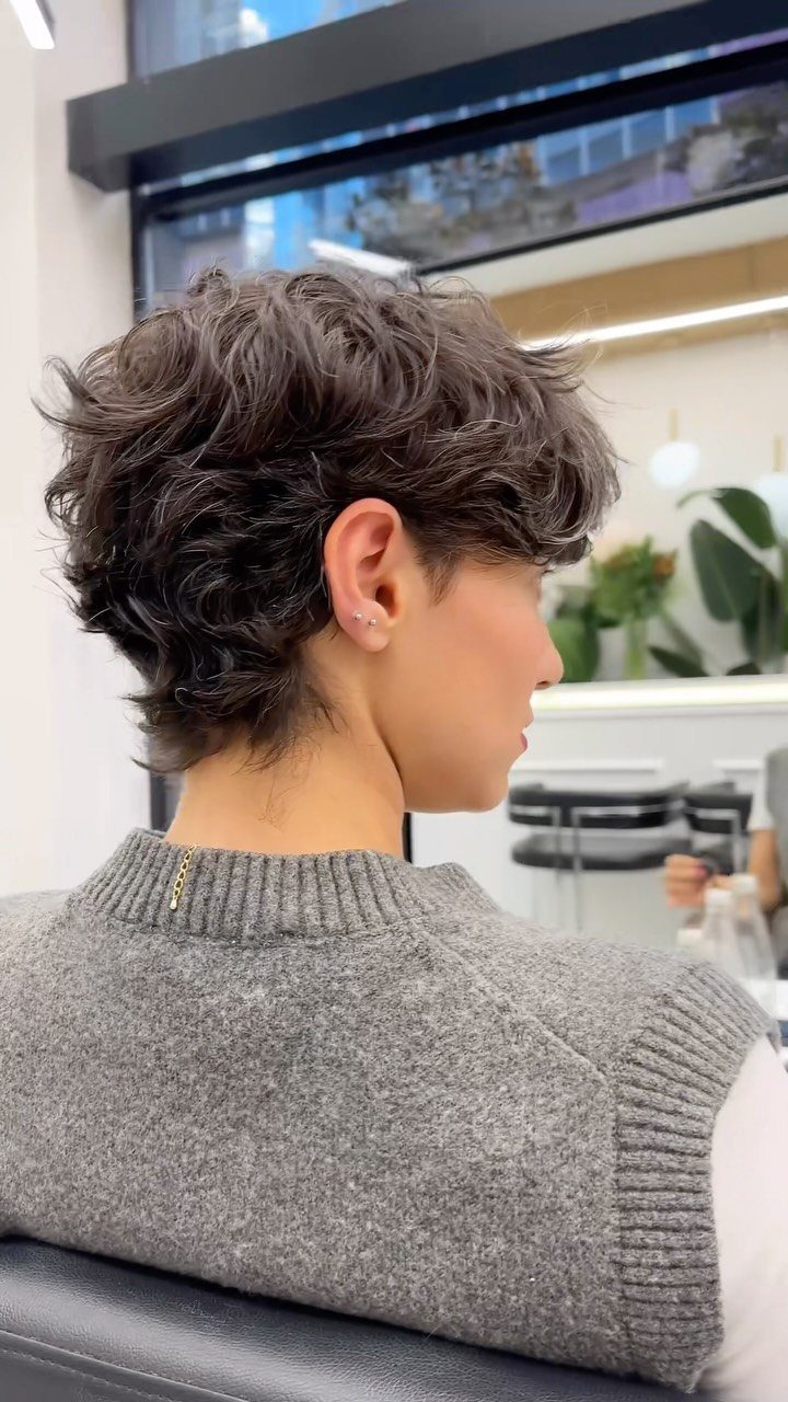 21 Short Curly Hair Styling Ideas for Every Texture 2 Person with a short, layered brown pixie cut with wavy texture in a salon.