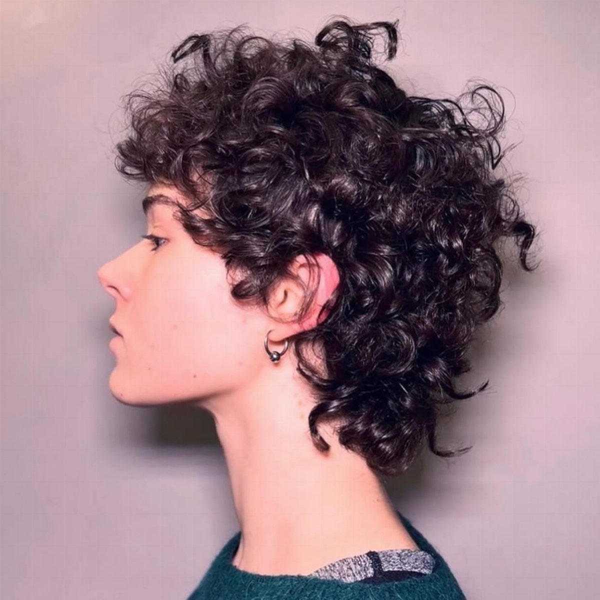 21 Short Curly Hair Styling Ideas for Every Texture 8 Person with short voluminous dark curly hair in a profile view against grey.