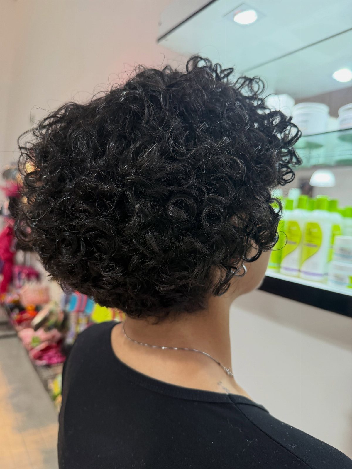 21 Short Curly Hair Styling Ideas for Every Texture 17 Woman with short voluminous black curly hair in a salon setting.