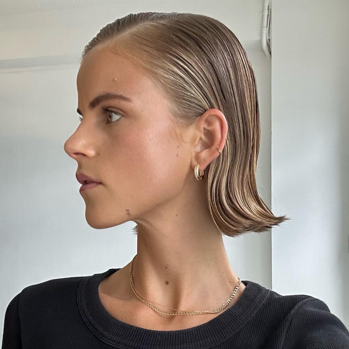 10 Sleek Hair Styles for Every Length and Occasion 5 Woman with a blonde slicked-back bob hairstyle wearing gold jewelry and black shirt.