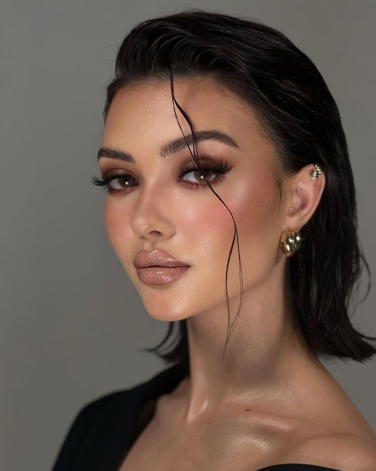 10 Sleek Hair Styles for Every Length and Occasion 4 Woman with dark slicked-back wet look hair and glowing makeup against grey background