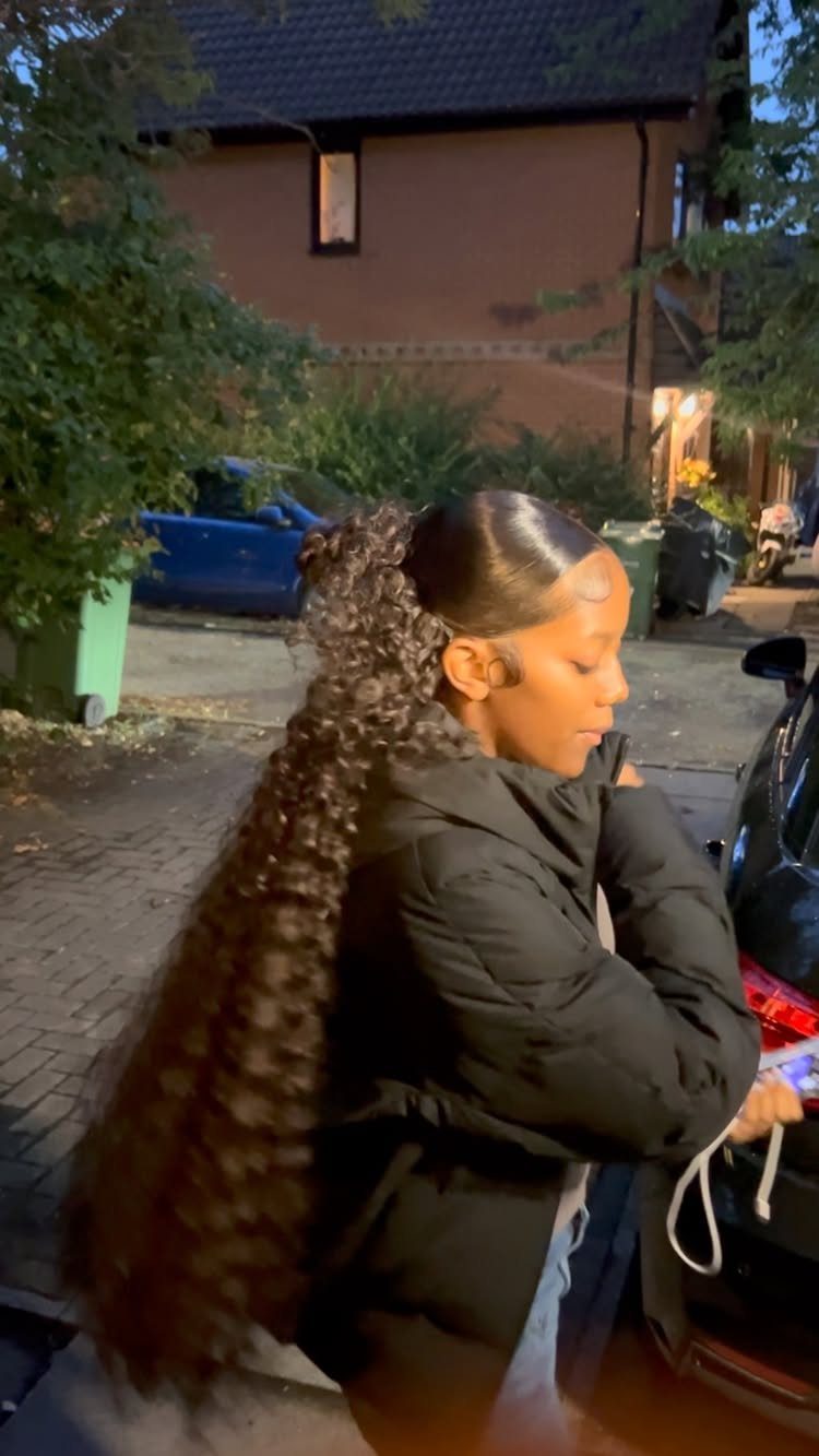 5 Slick Down Ponytail Ideas for Shine, Bangs and Curls 5 Woman with a very long, curly slicked-back ponytail wearing a black puffer jacket.