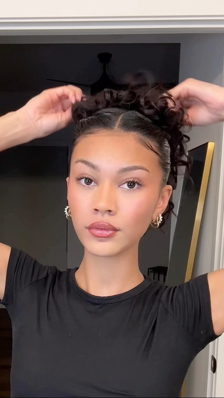 Slickback Messy Bun Ideas: 5 Easy Styles to Try 2 Woman arranging her dark curly hair into a bun on top of her head.