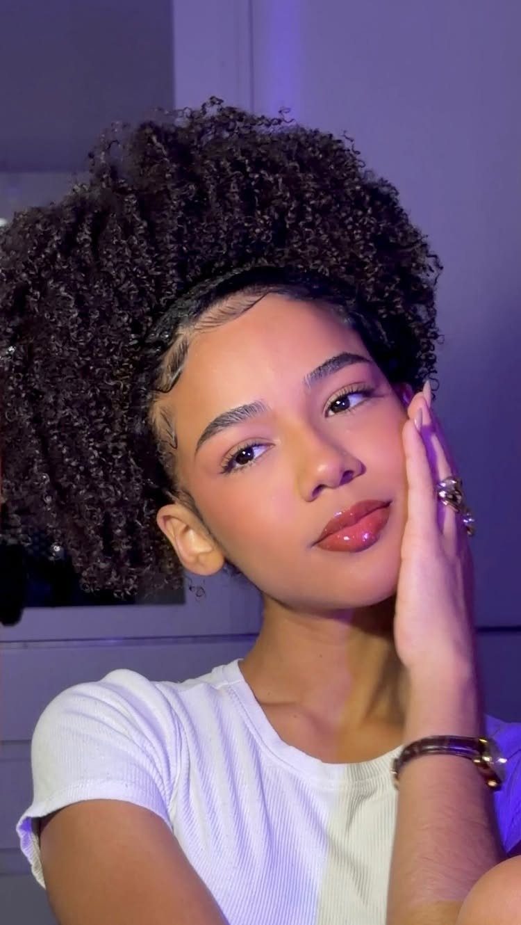 20 Thick Natural Hairstyles for Every Length and Mood 2 Woman with a voluminous natural afro hairstyle posing against a purple background.