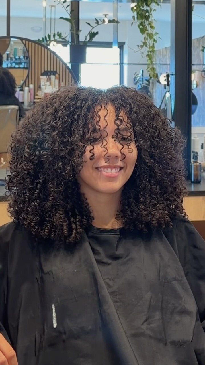 20 Thick Natural Hairstyles for Every Length and Mood 7 Woman with voluminous dark curly hair and curly bangs framing her face.