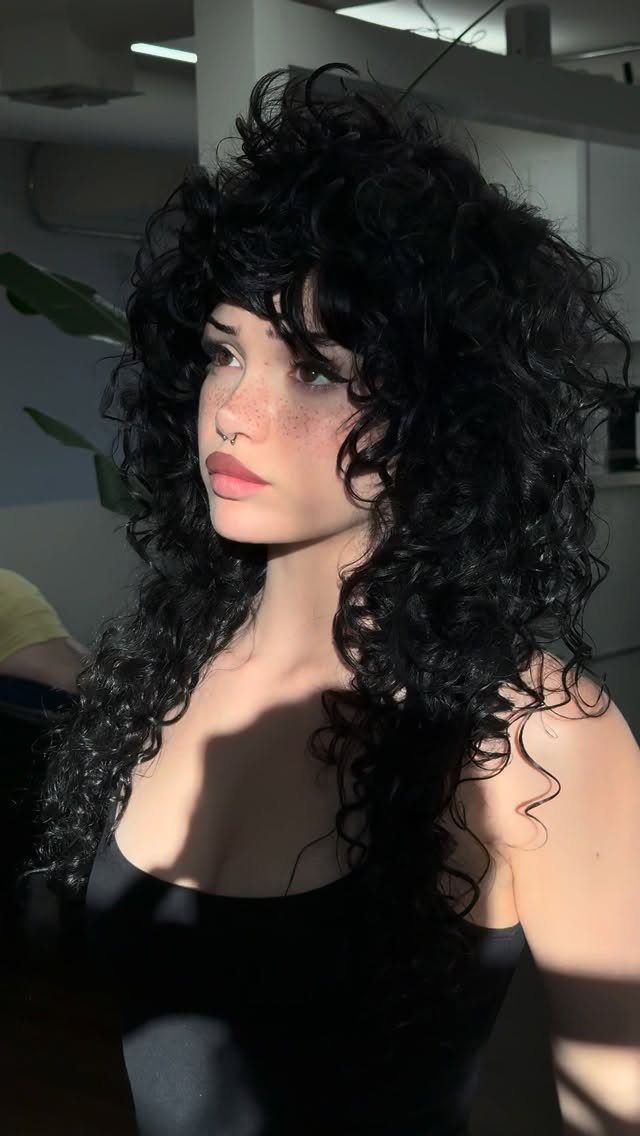 20 Thick Natural Hairstyles for Every Length and Mood 12 Woman with a voluminous black curly wolf cut hairstyle and matching curly bangs.