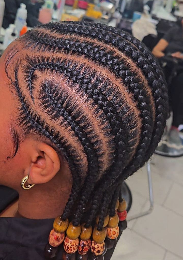 20 Thick Natural Hairstyles for Every Length and Mood 17 Curved cornrow braids with wooden beads on a person in a salon