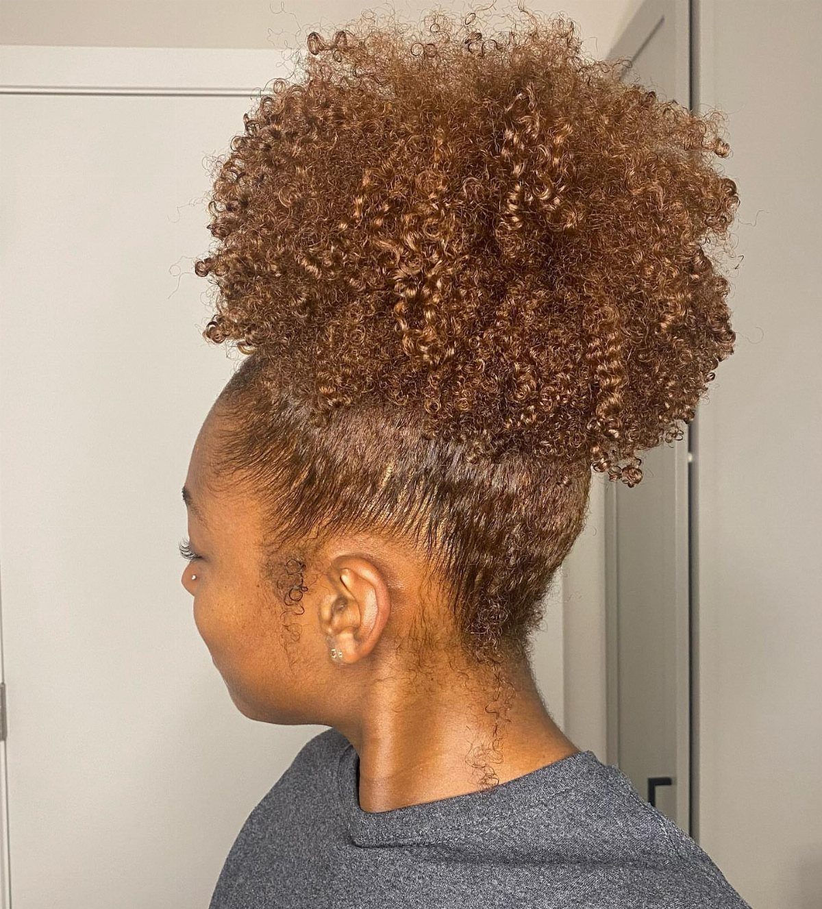 20 Thick Natural Hairstyles for Every Length and Mood 14 Woman with brown curly natural hair styled in a large high puff.