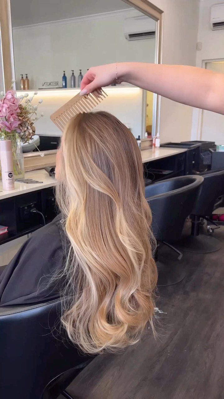 9 Toffee Caramel Hair Ideas for Brown and Blonde Bases 2 Long wavy toffee blonde hair being combed in a professional hair salon setting.