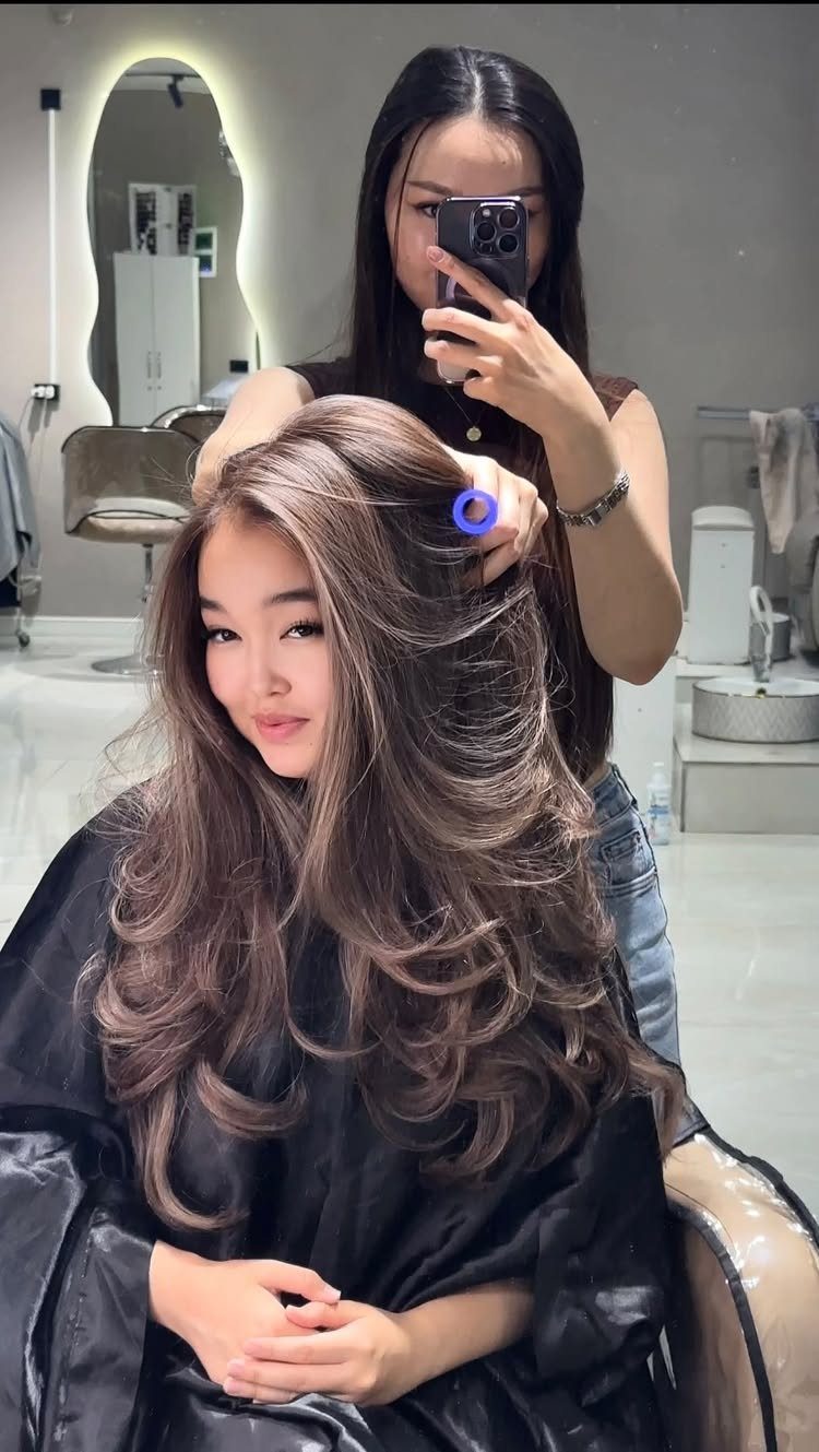 9 Toffee Caramel Hair Ideas for Brown and Blonde Bases 6 Woman with long wavy toffee caramel hair posing in a hair salon mirror
