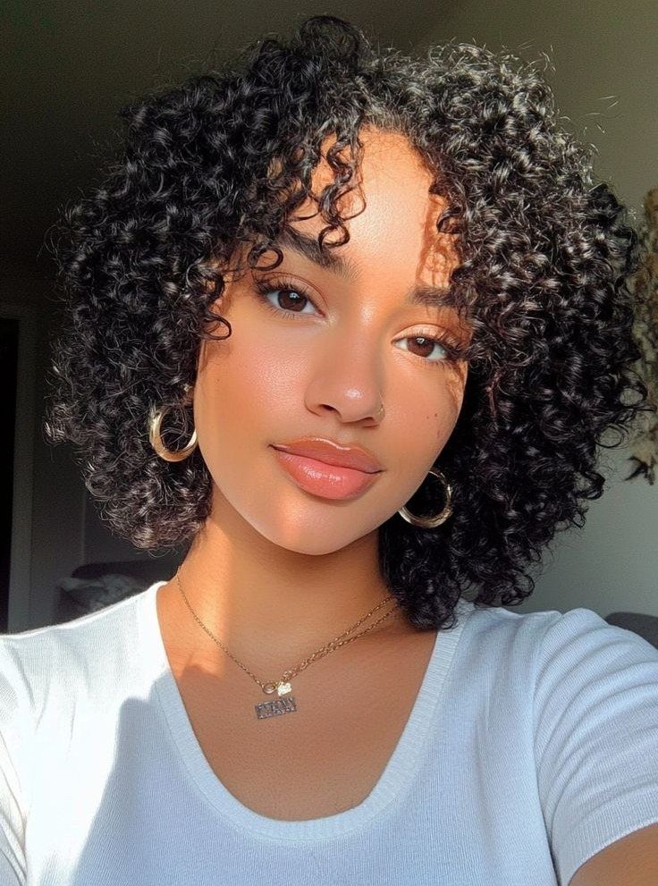 27 Trending Black Hairstyles, from Microbraids to Sisterlocks 10 Woman with a curly black afro bob wearing gold jewelry and white shirt