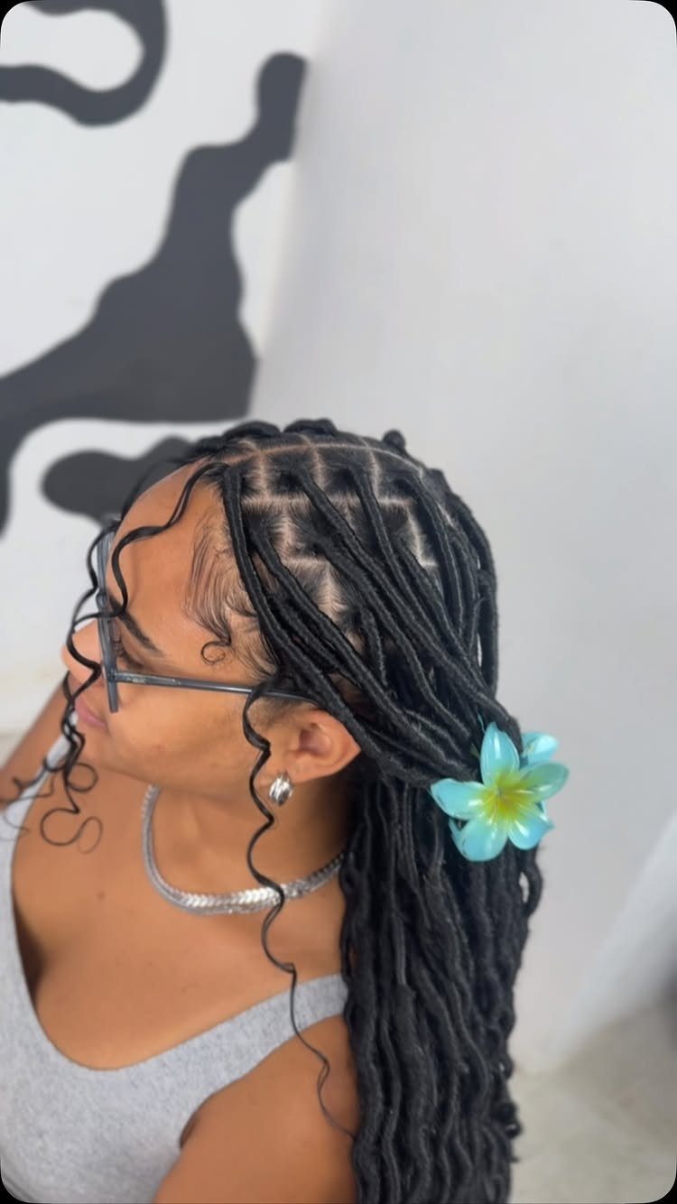 27 Trending Black Hairstyles, from Microbraids to Sisterlocks 5 Woman with long black faux locs and a blue flower in her hair.