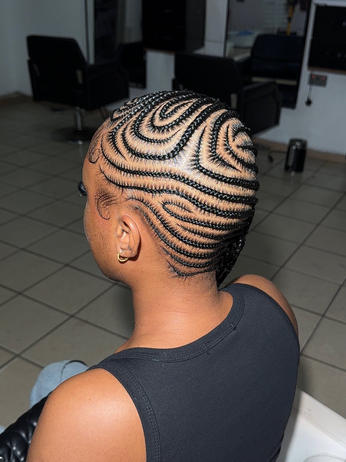 27 Trending Black Hairstyles, from Microbraids to Sisterlocks 25 Woman with curved cornrow braids swept to the side in a salon setting.