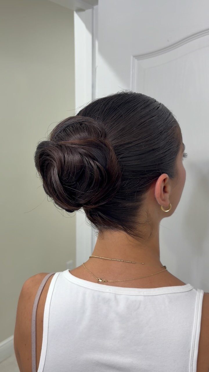 27 Trending Black Hairstyles, from Microbraids to Sisterlocks 9 Woman with dark hair styled in a sleek low bun wearing white top