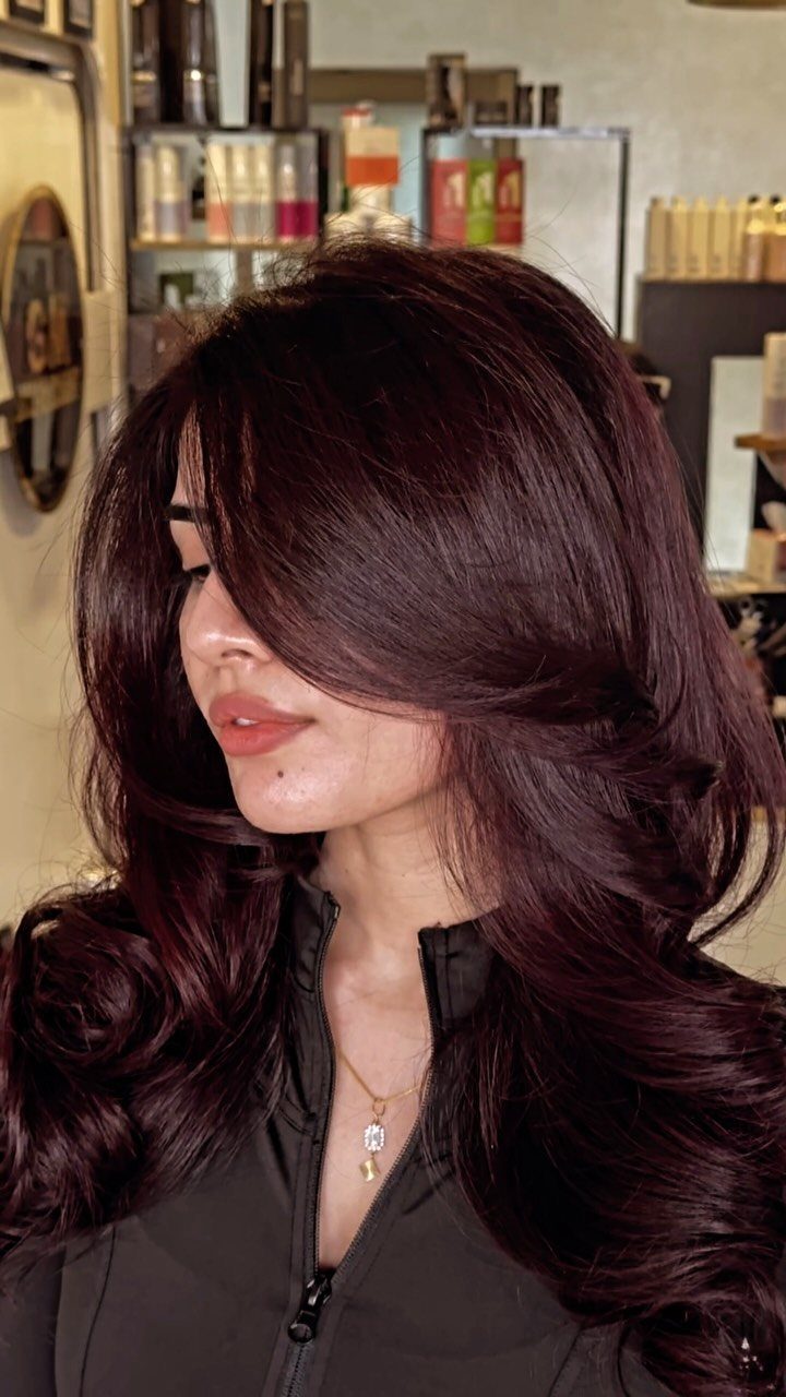 10 Violet Burgundy Hair Ideas for Dark to Bright Looks 1 Woman with long, voluminous deep burgundy hair styled in wavy layers in a salon.