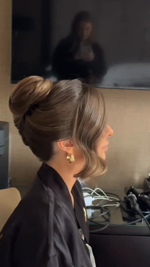 11 Wedding Guest Hairstyles for Medium Hair: Buns and Braids 9 Woman with brown hair in a high voluminous bun and face-framing curl.