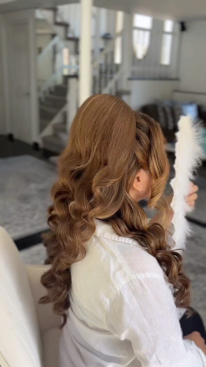 11 Wedding Guest Hairstyles for Medium Hair: Buns and Braids 4 Woman with voluminous light brown hair styled in large, polished curls from behind.