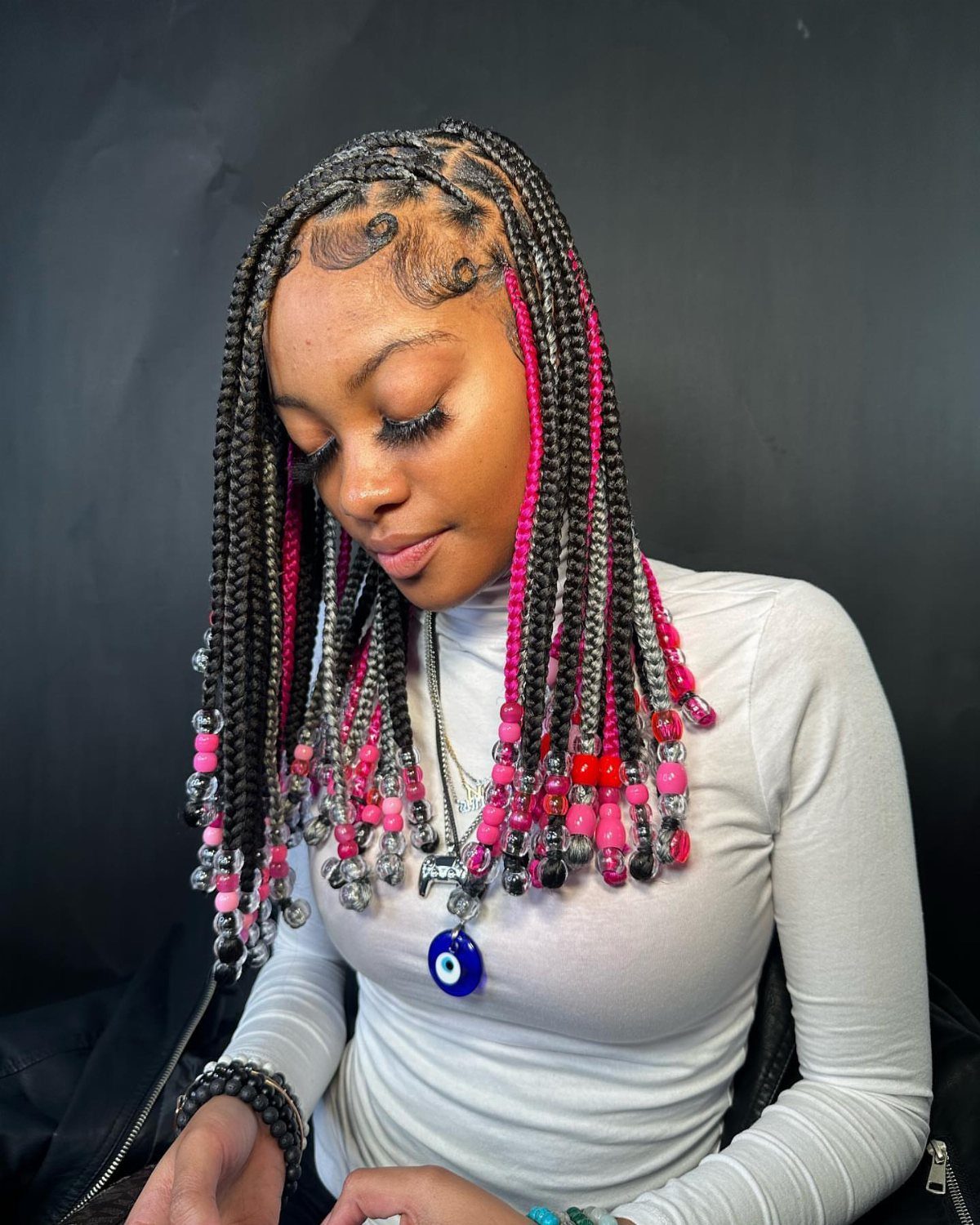 Y2K Braid Hairstyles: 9 Ideas From Butterfly Clips to Cornrows 4 Woman with black and pink box braids decorated with colorful beads at the ends.